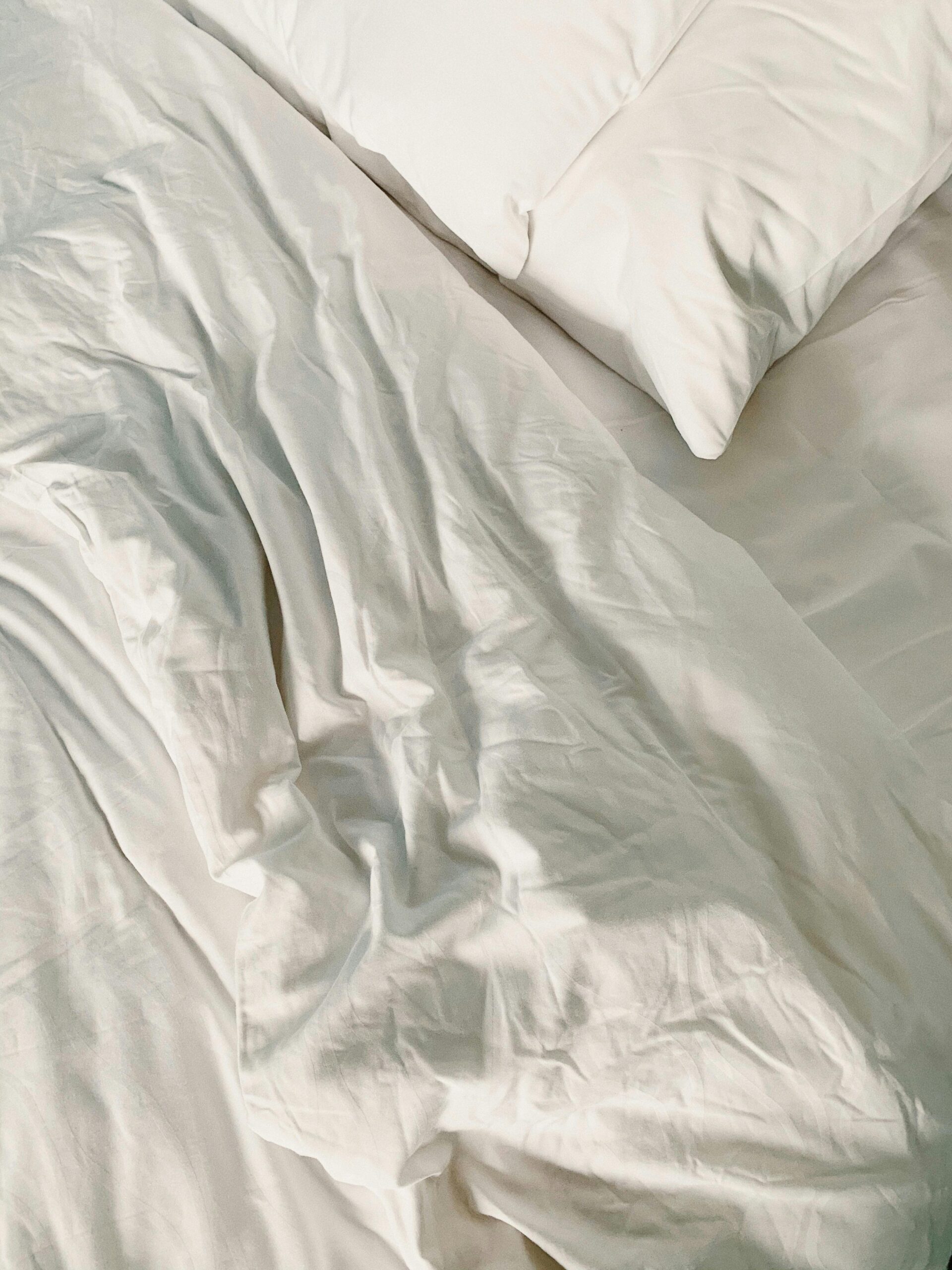 Close-up of white bed linen showcasing soft ripples and textures for a cozy, relaxing bedroom setting.