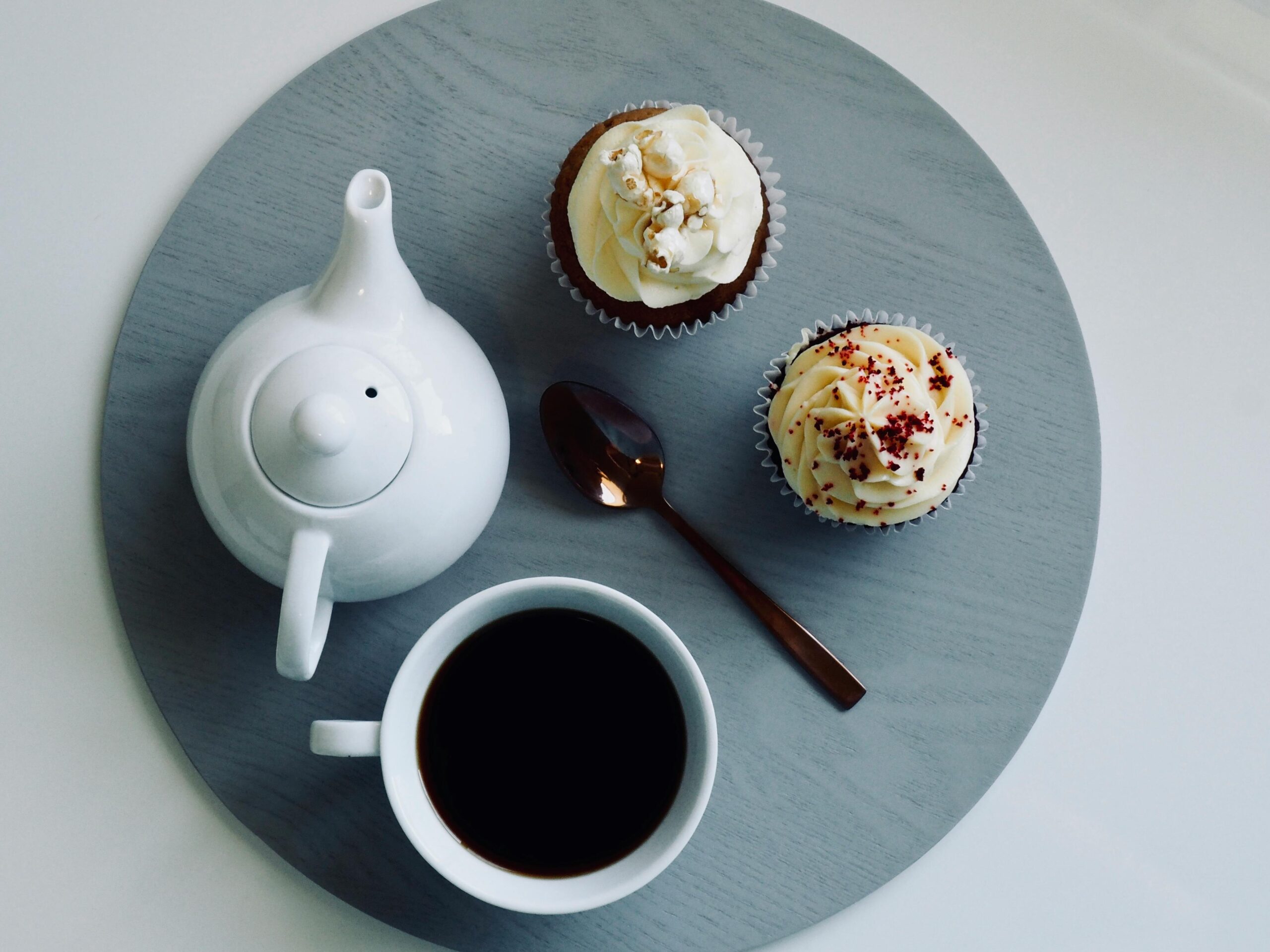 Flat lay of black coffee with delicious cupcakes on a round tray, styled for breakfast pleasure.